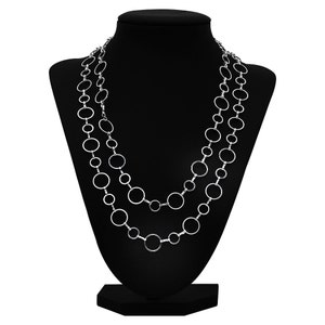 May include: A silver necklace with three layers of linked circles. The necklace is displayed on a black mannequin bust.