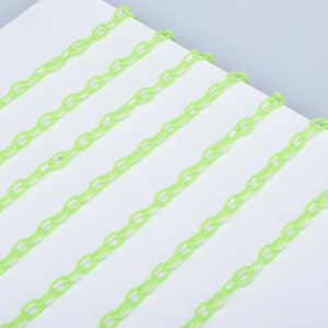 May include: A close-up of a bright green plastic chain. The chain is made of oval links and is laid out in parallel lines on a white surface.