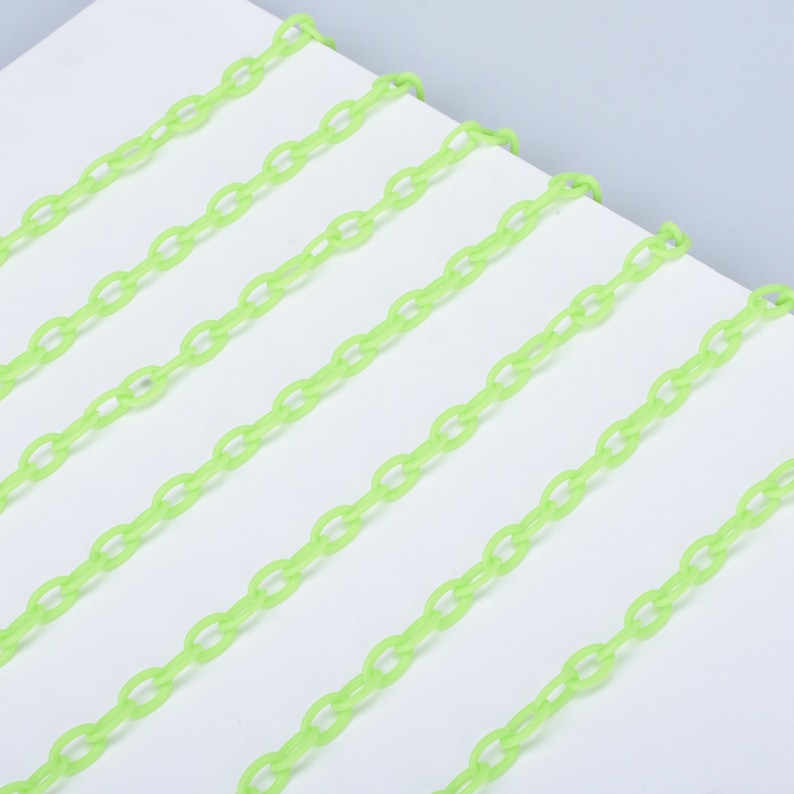 May include: A close-up of a bright green plastic chain. The chain is made of oval links and is laid out in parallel lines on a white surface.