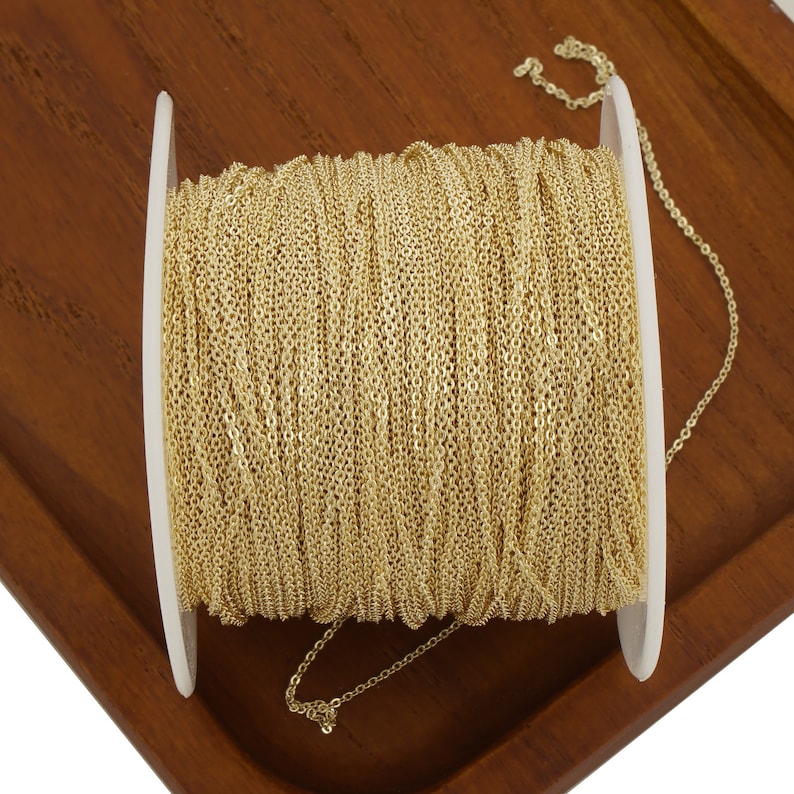 May include: A spool of gold-colored chain, wound around a white plastic spool. The chain is a delicate, fine-link style.