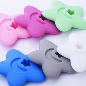 May include: Six silicone star-shaped teethers in different colors: pink, green, gray, white, blue, and purple. Each teether has a crescent moon shape with a small star in the center.