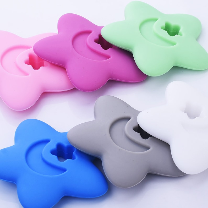 May include: Six silicone star-shaped teethers in different colors: pink, green, gray, white, blue, and purple. Each teether has a crescent moon shape with a small star in the center.