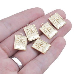 Puede incluir: Cinco dijes de palmera de color dorado con un diseño detallado. Los dijes son rectangulares y tienen una superficie ligeramente texturizada.