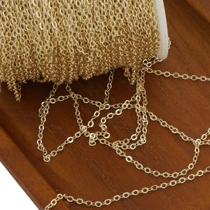 May include: A spool of gold chain, with a portion of the chain unraveled and lying on a wooden surface.