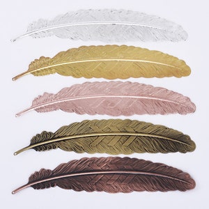 Könnte beinhalten: Fünf Metall-Lesezeichen in Form von Federn in verschiedenen Farben: Silber, Gold, Roségold, Bronze und Kupfer. Jedes Lesezeichen hat ein detailliertes Federdesign.