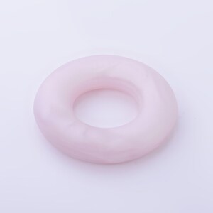 May include: A pale pink donut-shaped ring made of smooth, polished stone.