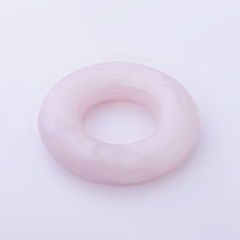 May include: A pale pink donut-shaped ring made of smooth, polished stone.