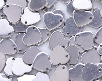 May include: A large quantity of silver metal heart-shaped charms with a hole at the top. The charms are scattered on a white surface.