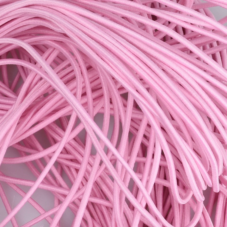 May include: A close-up of a pile of pink elastic cord. The cord is soft and stretchy, and it is ideal for crafting projects.