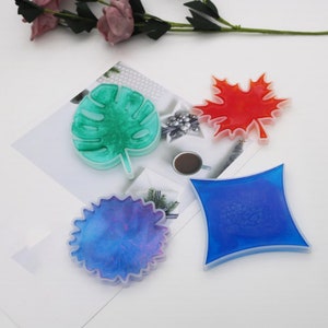 May include: Four silicone molds for resin casting, featuring a green monstera leaf, a red maple leaf, a blue round shape with a textured surface, and a blue diamond shape.
