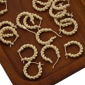 May include: A group of gold-toned hoop earrings with a twisted rope design. The earrings are arranged on a wooden surface.
