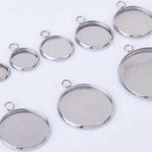 May include: A set of eight silver-toned metal pendant trays with round bezels. The trays are of varying sizes and are perfect for creating custom jewellery.