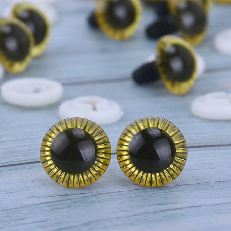 May include: Two large, black plastic eyes with gold trim. The eyes are round and have a shiny finish. They are commonly used for craft projects.