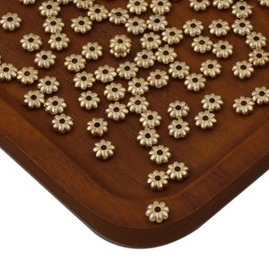 May include: A large quantity of gold-colored metal flower-shaped beads. The beads are scattered on a wooden surface.