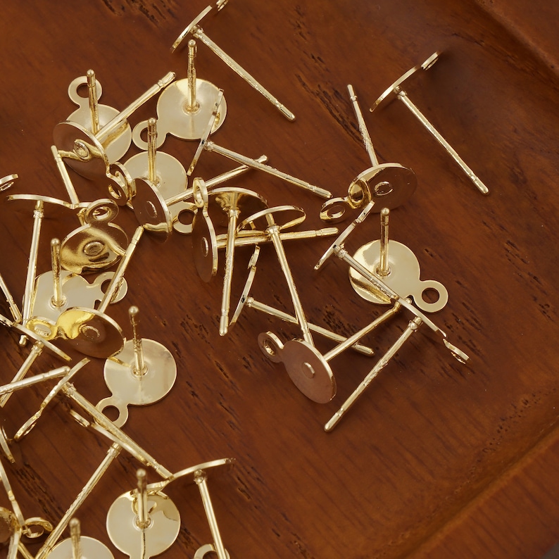 May include: A close-up of a pile of gold-toned earring findings. The findings are made of metal and have a small loop at the top. They are designed to be used with a variety of earring styles.