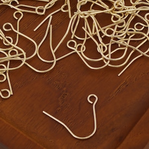 Puede incluir: Primer plano de un mont&oacute;n de ganchos para pendientes de color dorado. Los ganchos son de metal y tienen un dise&ntilde;o sencillo y cl&aacute;sico.