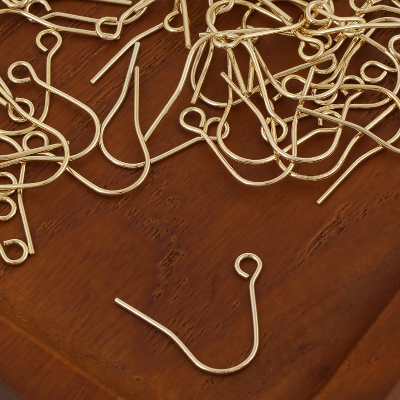 Puede incluir: Primer plano de un mont&oacute;n de ganchos para pendientes de color dorado. Los ganchos son de metal y tienen un dise&ntilde;o sencillo y cl&aacute;sico.