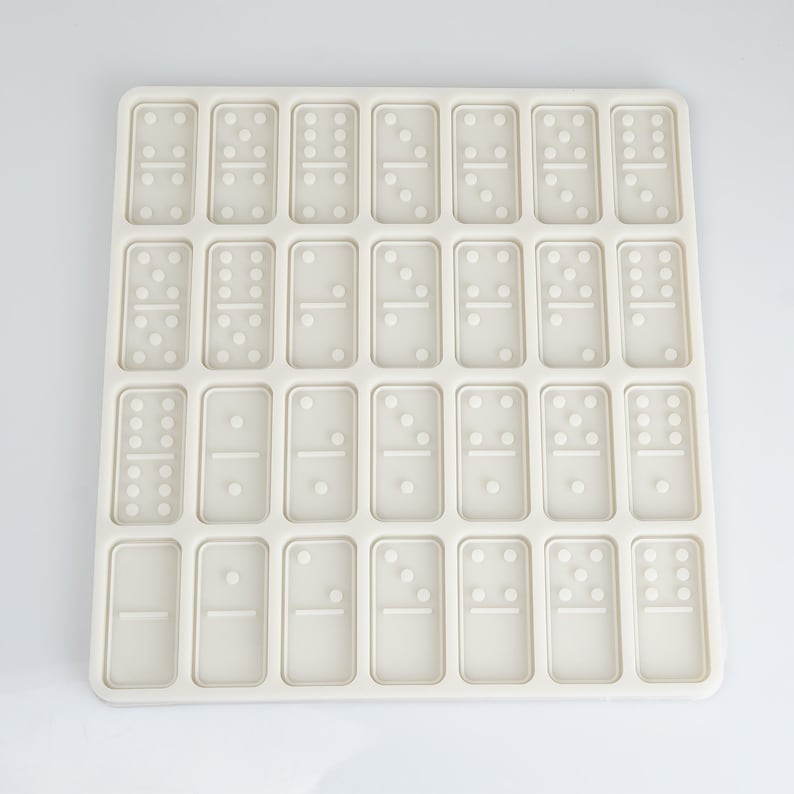 May include: White silicone mold with 28 individual cavities shaped like dominoes. The mold is designed for making chocolate or candy dominoes.