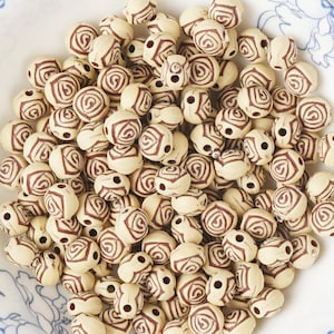 May include: A collection of cream-colored, round beads with a dark brown rose pattern. The beads are scattered, showing their detailed design. These beads are suitable for jewelry making and crafts.