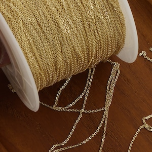 May include: A spool of gold-colored chain, with a portion of the chain unraveled and lying on a wooden surface.