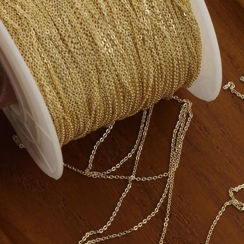 May include: A spool of gold-colored chain, with a portion of the chain unraveled and lying on a wooden surface.