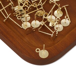 May include: A pile of gold-toned earring posts with a loop on the back. The posts are on a wooden surface.
