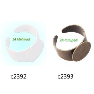 May include: Two rings with a 14 mm pad for attaching a cameo or other embellishment. The ring on the left is white plastic and the ring on the right is antique brass.
