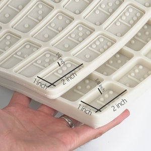 May include: White silicone mold for making dominoes. The mold is 2 inches wide and 1 inch tall. Each domino is 1/4 inch thick and 3/8 inch tall.