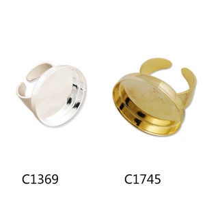 May include: Two ring blanks, one silver and one gold, for jewellery making. The ring blanks are round and have a flat surface for adding embellishments. The silver ring blank is labelled C1369 and the gold ring blank is labelled C1745.