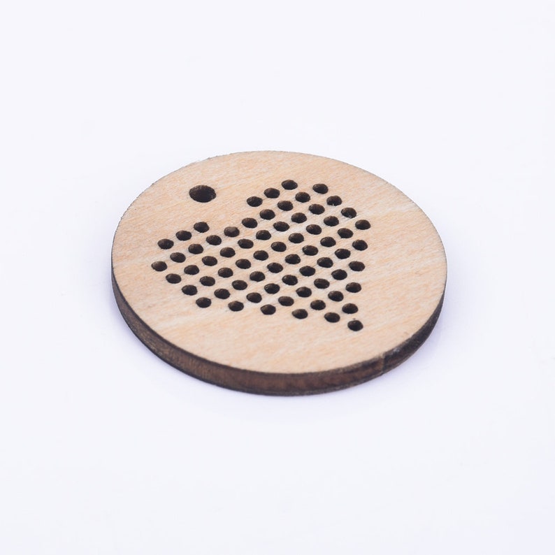 Puede incluir: Un disco redondo de madera con un patr&oacute;n de coraz&oacute;n de agujeros para bordado de punto de cruz. El disco tiene un peque&ntilde;o agujero en la parte superior para colgar.