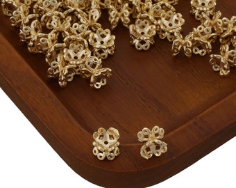 Peut inclure: Un tas de capsules de perles en métal doré sur une surface en bois. Les capsules de perles sont en forme de fleur avec un trou au centre. Il y a deux capsules de perles sur le côté droit de l'image.