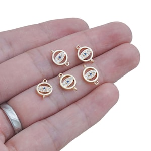 Puede incluir: Seis colgantes de ojo turco de tono dorado con detalles de cristal transparente y azul. Cada colgante tiene un bucle a cada lado para sujetarlo a una cadena o pulsera.