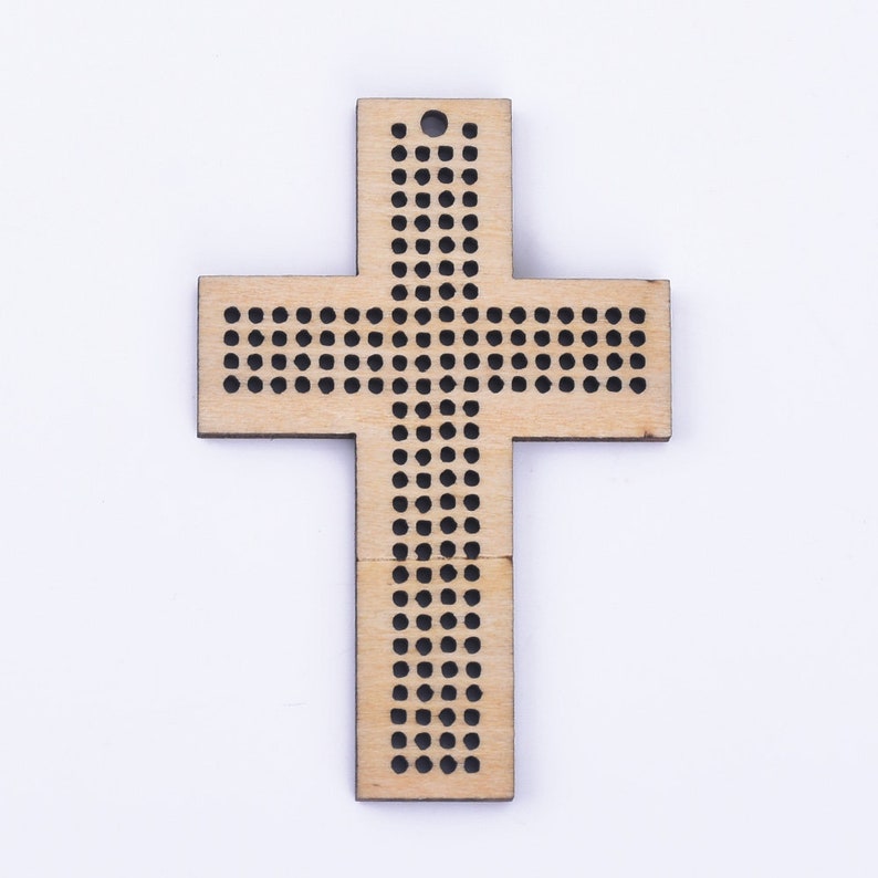 Puede incluir: Una cruz de madera con un agujero en la parte superior para colgar. La cruz est&aacute; decorada con una cuadr&iacute;cula de peque&ntilde;os c&iacute;rculos negros.