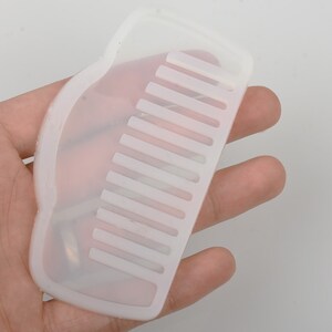 May include: A white silicone comb with a curved handle. The comb has a row of teeth on one side.