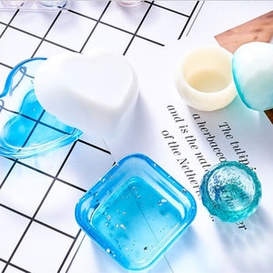 Op de afbeelding: Een set van vier blauwe harsvormen voor het maken van sieraden of andere knutselwerkjes. De vormen zijn in de vorm van een hart, een vierkant en twee ronde vormen. De vormen bevinden zich op een witte rasterachtergrond.