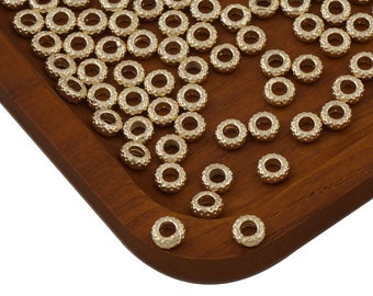 May include: A large quantity of gold-colored metal beads with a textured surface. The beads are arranged on a wooden surface.