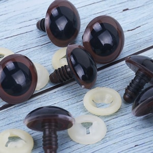 May include: A collection of brown and black plastic safety eyes for crafts, with matching white plastic washers. The eyes have a glossy finish and are designed to be securely attached to fabric or other materials.