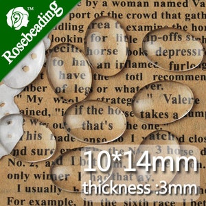 May include: Oval-shaped glass beads, 10mm by 14mm, with a thickness of 3mm. The beads are clear and magnify the text underneath. The text reads "10*14mm thickness:3mm".