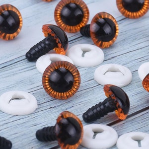 May include: A close-up of a group of orange and black plastic safety eyes with a black plastic washer. The eyes are used for craft projects and are available in a variety of sizes.