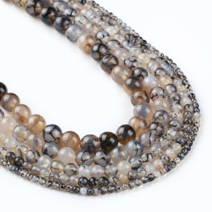 May include: A strand of grey agate beads with black dendritic patterns. The beads are round and vary in size. The strand is on a white background.