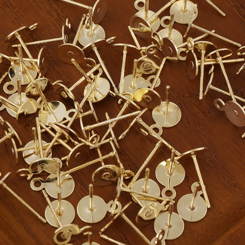 May include: A pile of gold-toned earring posts with loops. The posts are made of metal and have a round base. The loops are small and are located at the top of the posts.