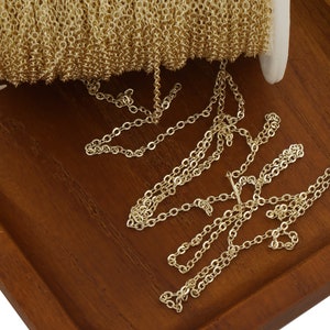 May include: A spool of gold-colored chain, with a portion of the chain unraveled and lying on a wooden surface.