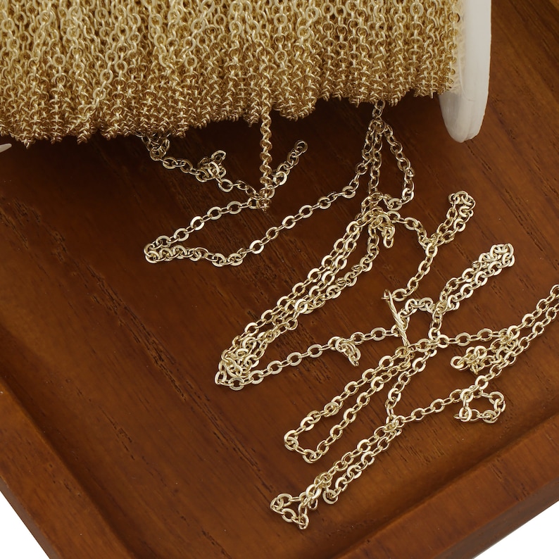 May include: A spool of gold-colored chain, with a portion of the chain unraveled and lying on a wooden surface.