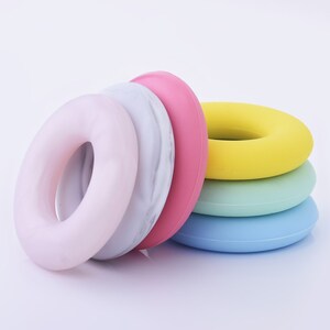 May include: A set of five colorful silicone rings, stacked in a graduated size order. The rings are in shades of pink, yellow, green, and blue. The top ring is a light gray with a marble pattern.