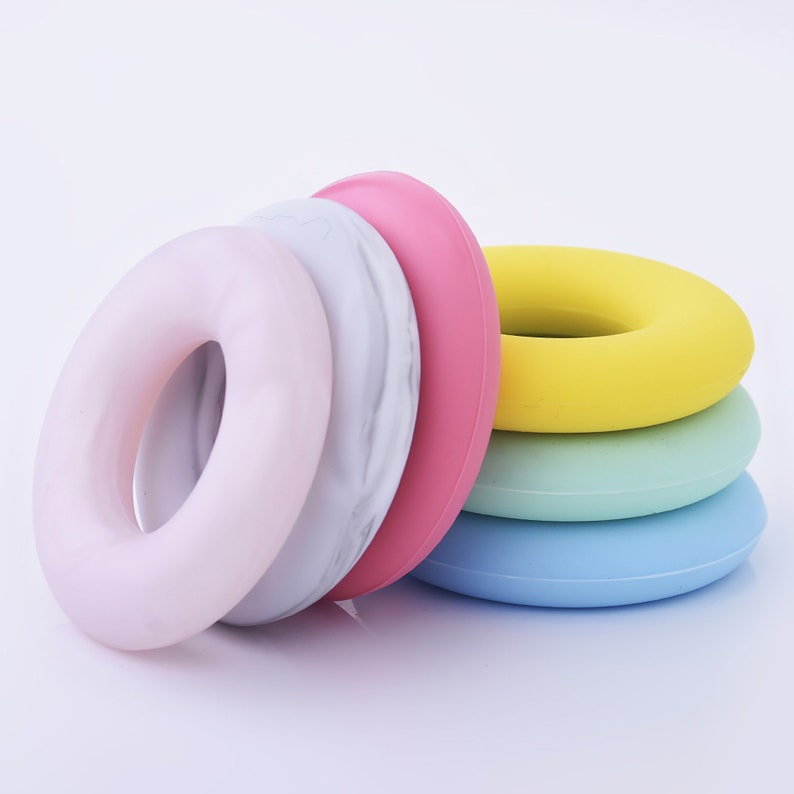 May include: A set of five colorful silicone rings, stacked in a graduated size order. The rings are in shades of pink, yellow, green, and blue. The top ring is a light gray with a marble pattern.