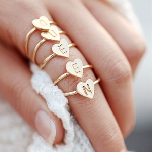 May include: Four gold rings with heart-shaped tops, each featuring a different letter. The letters are L, L, N, and U.