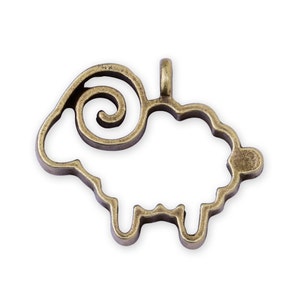 Puede incluir: Un amuleto de metal de color bronce en forma de oveja con un cuerno en espiral. El amuleto es hueco y tiene un bucle en la parte superior para sujetarlo a un collar o pulsera.