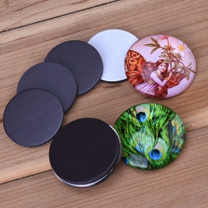 May include: A set of round black magnetic discs and two round glass cabochons with printed designs. One cabochon features a fairy with butterfly wings and flowers, the other features a peacock feather design.