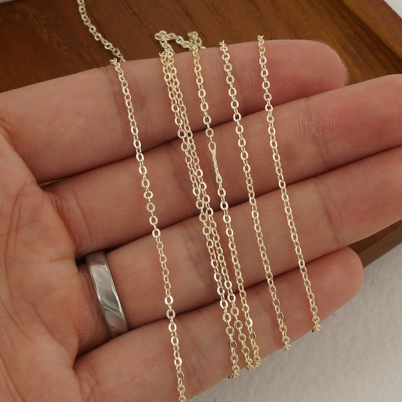 May include: Five gold chains of different lengths and thicknesses, laid out on a hand.