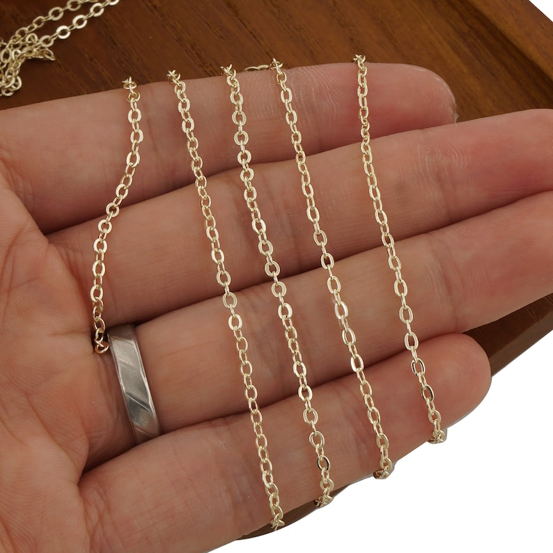May include: Four strands of gold chain, varying in length, are displayed on a hand. The chains are delicate and have a smooth, polished finish.